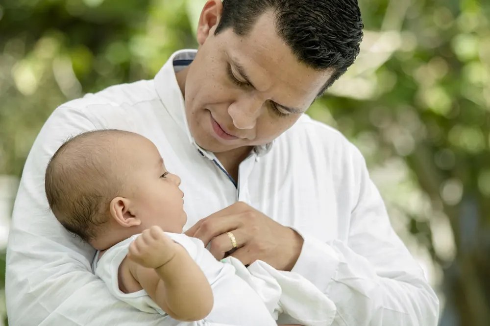 Homme tenant un bébé contre lui en extérieur, échange de regard tendre