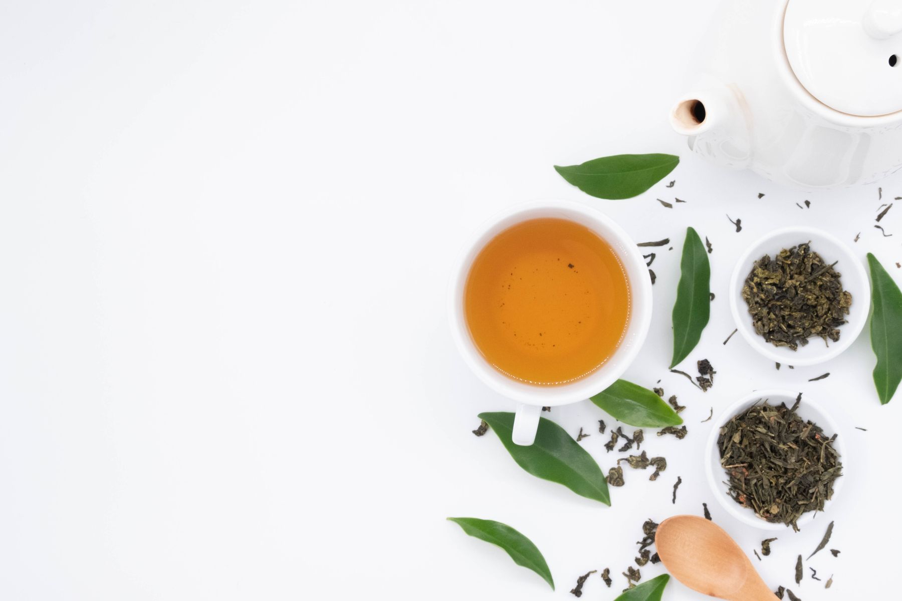 tasse de thé vert infusé entourée de feuilles fraîches et de feuilles séchées sur fond blanc